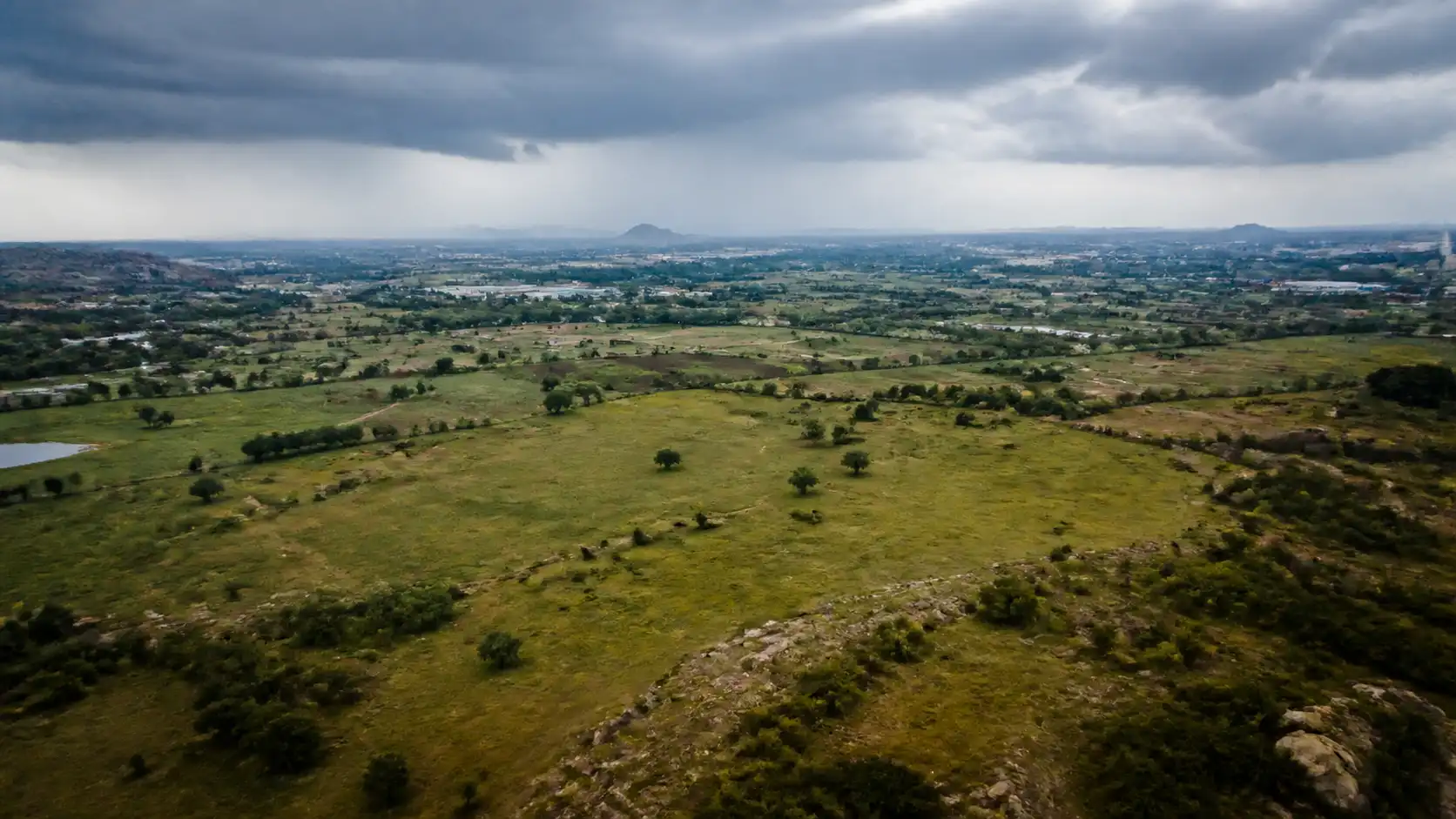 Conceptual aerial view of open land and distant infrastructure under monsoon clouds